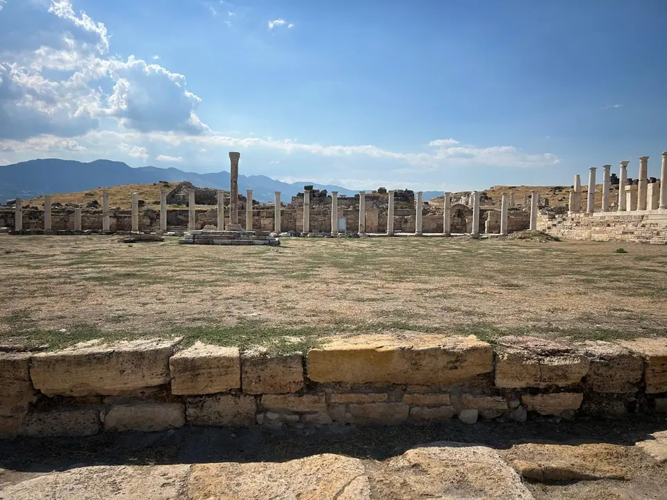 Standing columns of a colonnaded street at Tripolis, dry grass in front, mountains and a wide blue sky behind