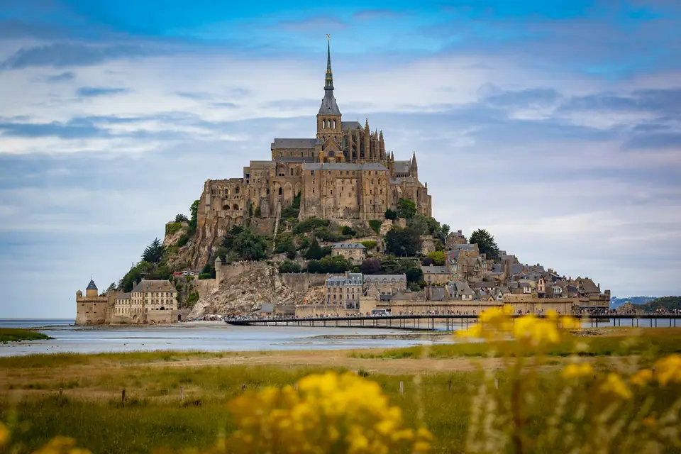Mont-Saint-Michel abbey on its rocky island rising above wet sand flats at low tide, with the causeway bridge leading to it