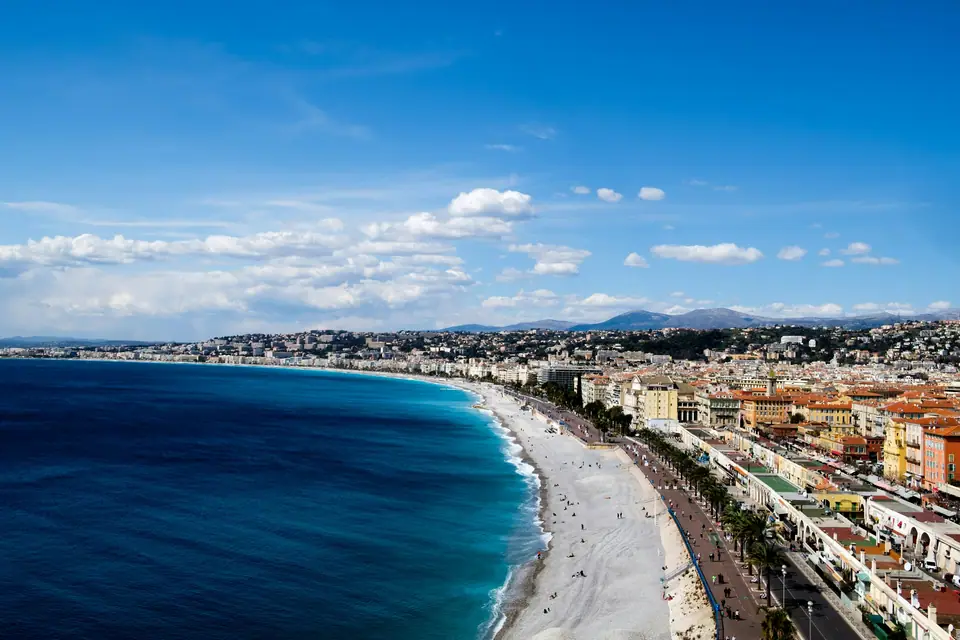 The curved pebble beach and turquoise sea of the Baie des Anges in Nice, with the Promenade des Anglais and pastel buildings along the shore