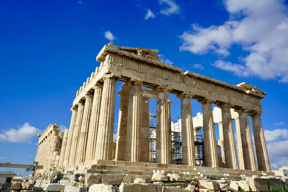 The Parthenon on the Acropolis hill in Athens, its marble columns lit by afternoon sun under a clear blue sky