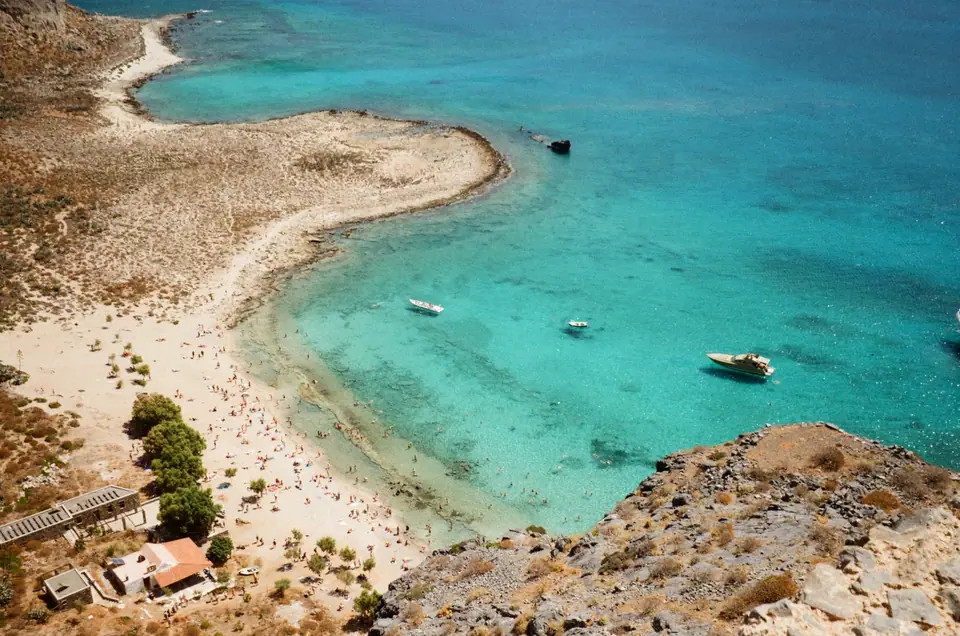 Clear turquoise sea and a pale sandy beach below rocky hills on the coast of Crete