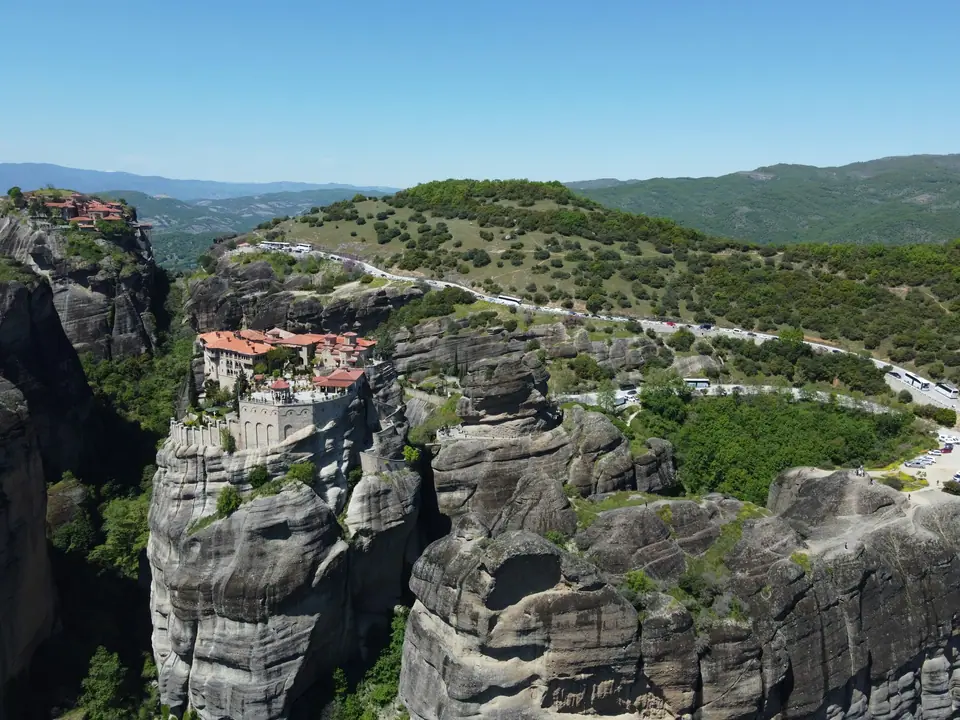 Monasteries perched on top of tall grey rock pillars at Meteora, with the green plain of Thessaly spread out below