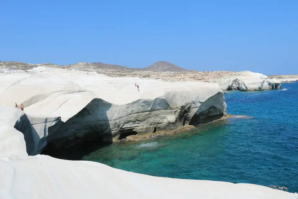 White volcanic rock formations curving down into turquoise water at Sarakiniko beach on Milos
