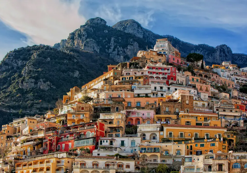 Pastel houses stacked on a steep cliff above the sea on the Amalfi Coast, with small boats in the bay below