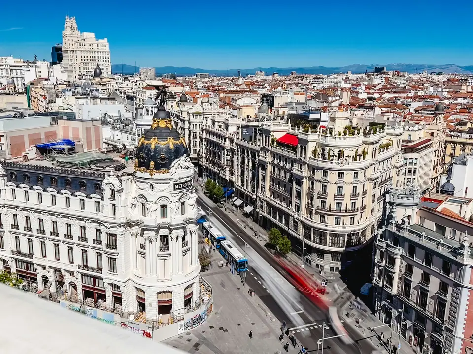 The Gran Vía in central Madrid with its grand early 20th century buildings, the domed Metrópolis building on the corner and traffic in the wide street below