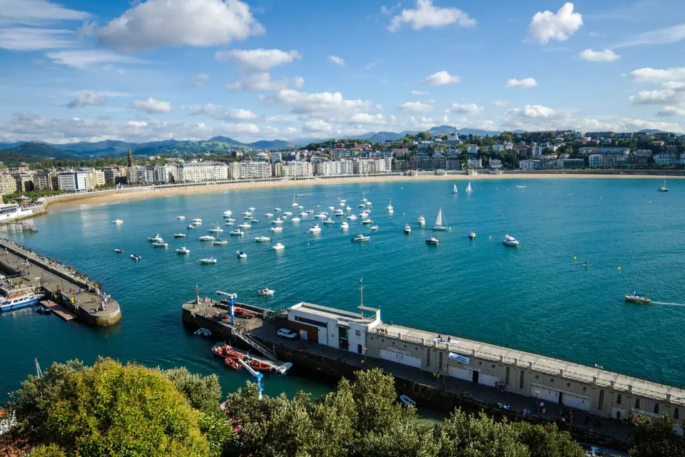 The curved sandy beach of La Concha in San Sebastián, with the old town, the green Monte Urgull and boats moored in the calm bay