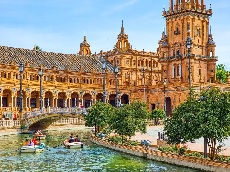 The Plaza de España in Seville, a vast semicircular brick building with towers at each end, a canal crossed by tiled bridges in front of it