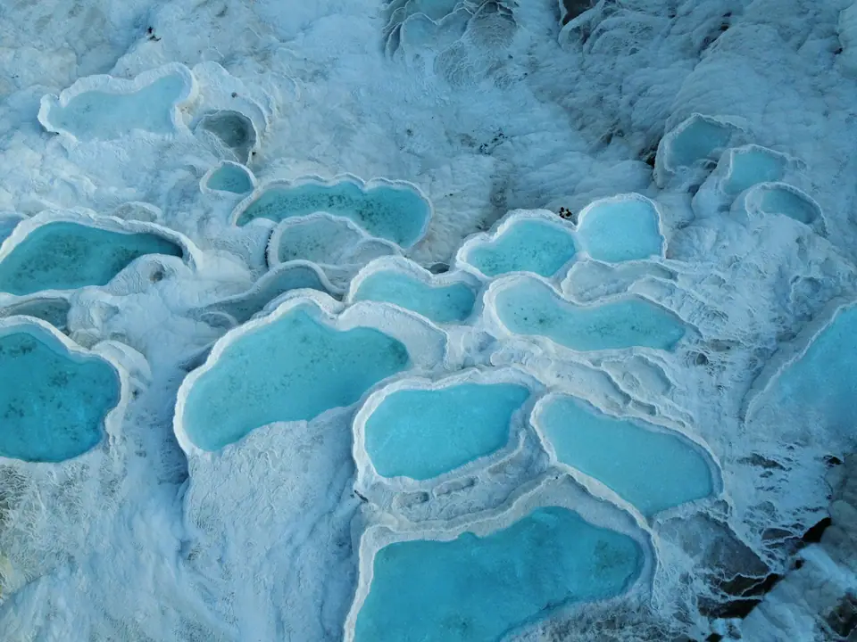 The white travertine terraces of Pamukkale with shallow pools of pale blue water, the valley and mountains in the distance