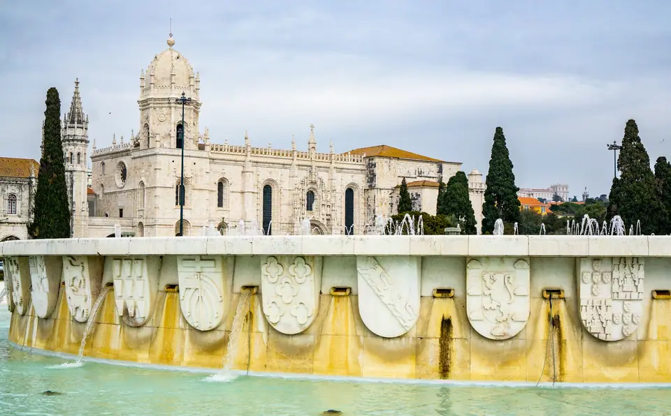 Jerónimos Monastery in Belém behind a fountain and cypress trees