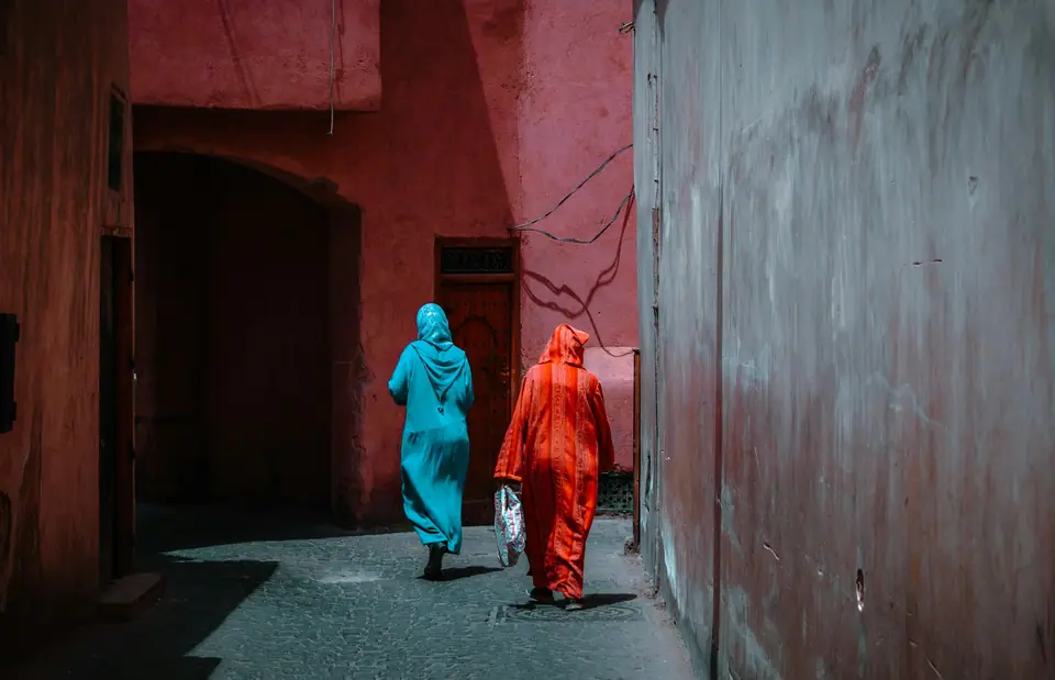 Two people in long clothes walking down a pink-walled lane in the medina