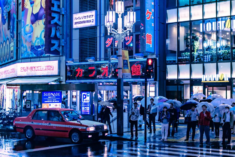 People with umbrellas at a rainy Tokyo crossing at night
